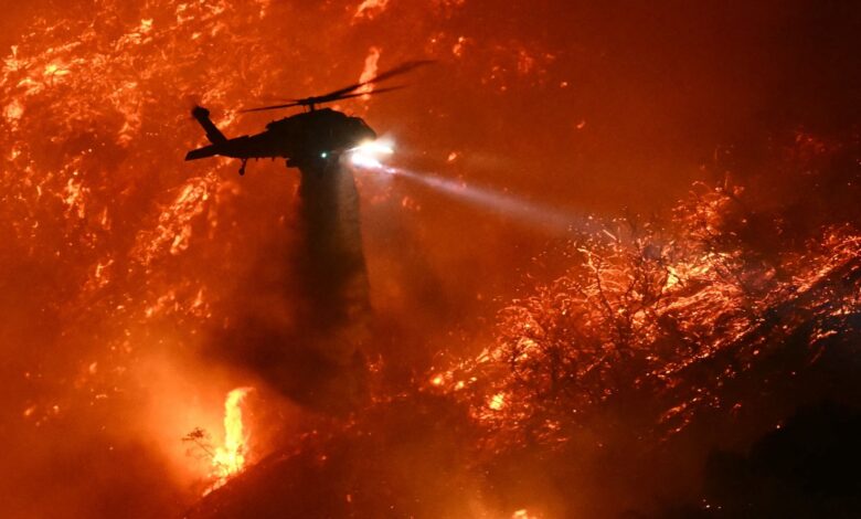 A helicopter drops water over a raging wildfire.