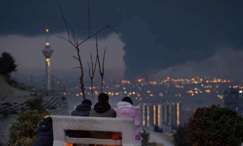 View overlooking Tehran with giant smoke cloud over city with four children on a bench watching the scene.
