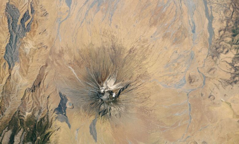 Satellite picture of a dry region with a volcano capped with white ash